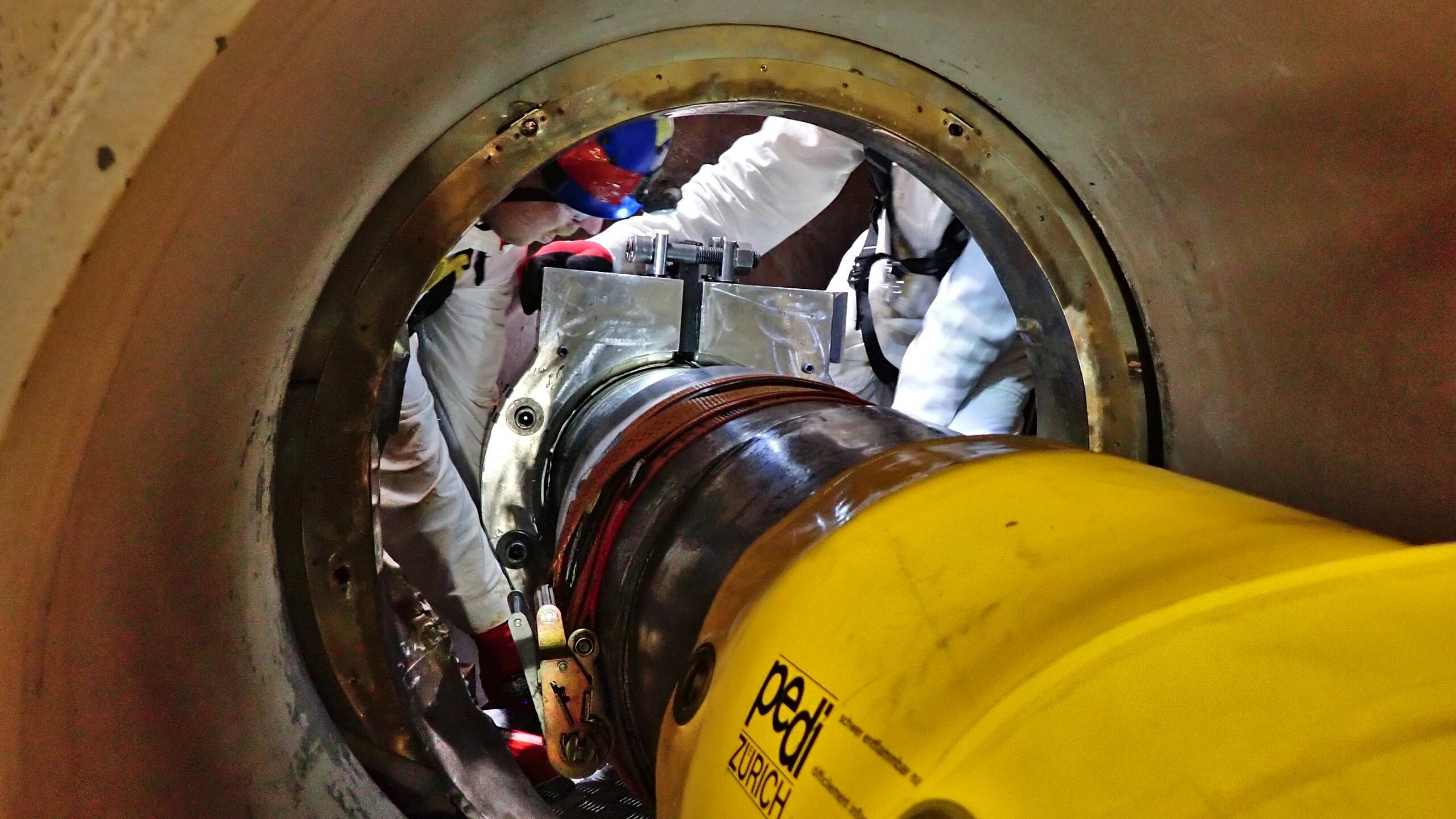 Technicians in protective suits working on heavy equipment inside a large circular opening