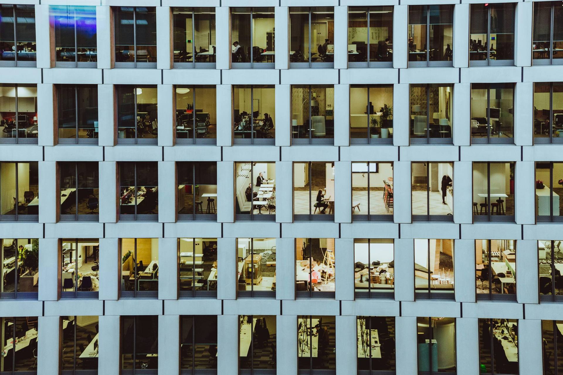 A grid of lit office windows at night, with people working inside
