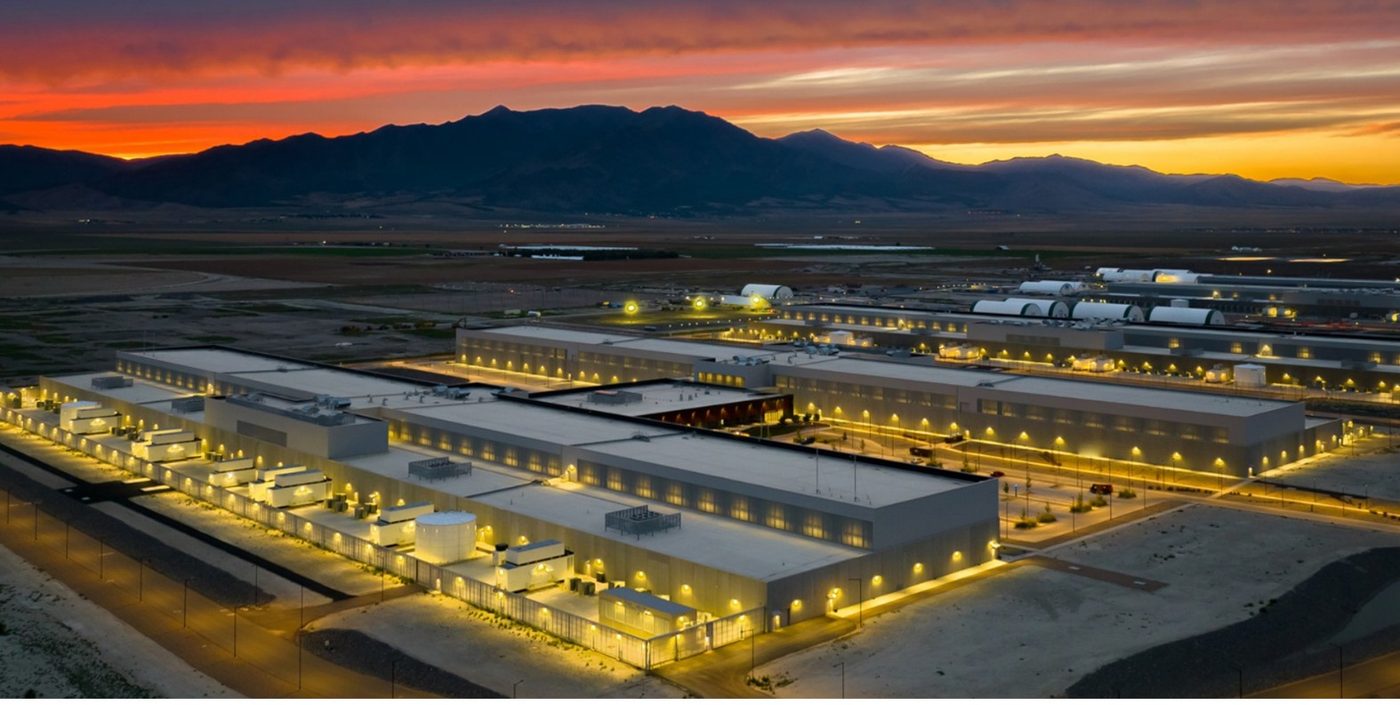A data center campus lit at dusk beneath a mountain range