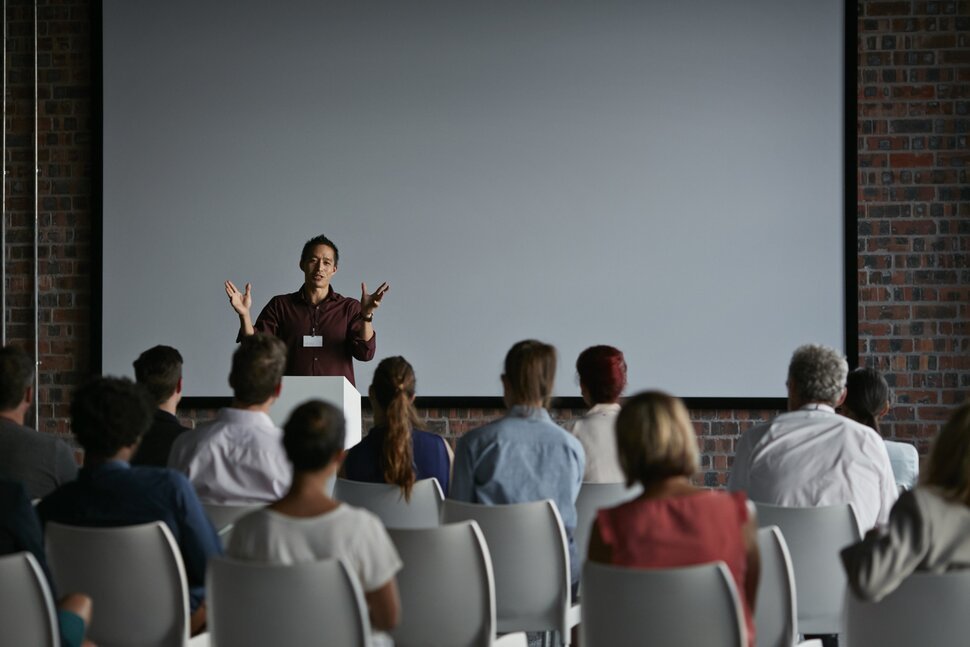 A speaker presenting to a seated public audience